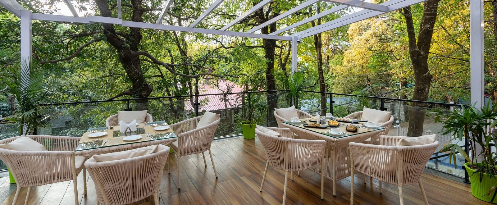 The deck at DLS The Emerald, Nainital with chairs and tables with the background of trees and greenery