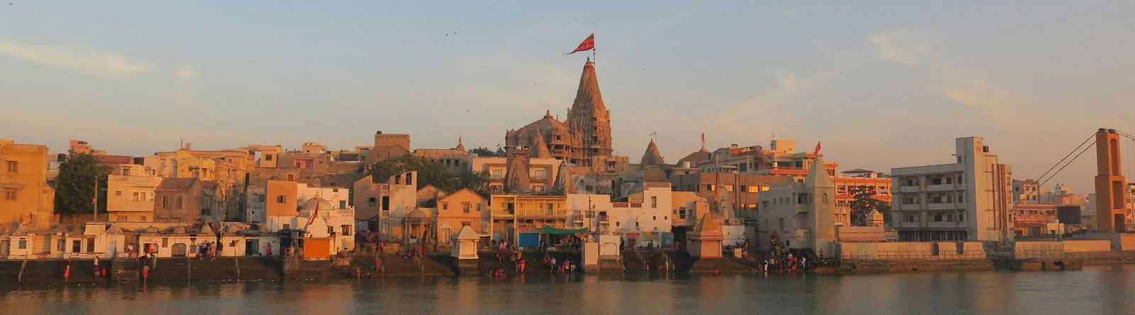 A wide angle shot of a river bank with small temples and establishment with a serene river flowing in front of them.