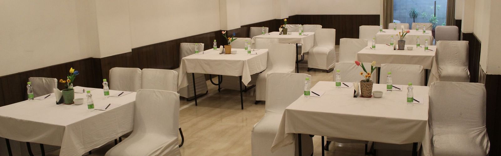 An image of a banquet hall at Inde Hotels Vista Woods featuring several sets of chairs and table where water bottles and flower pots are placed 