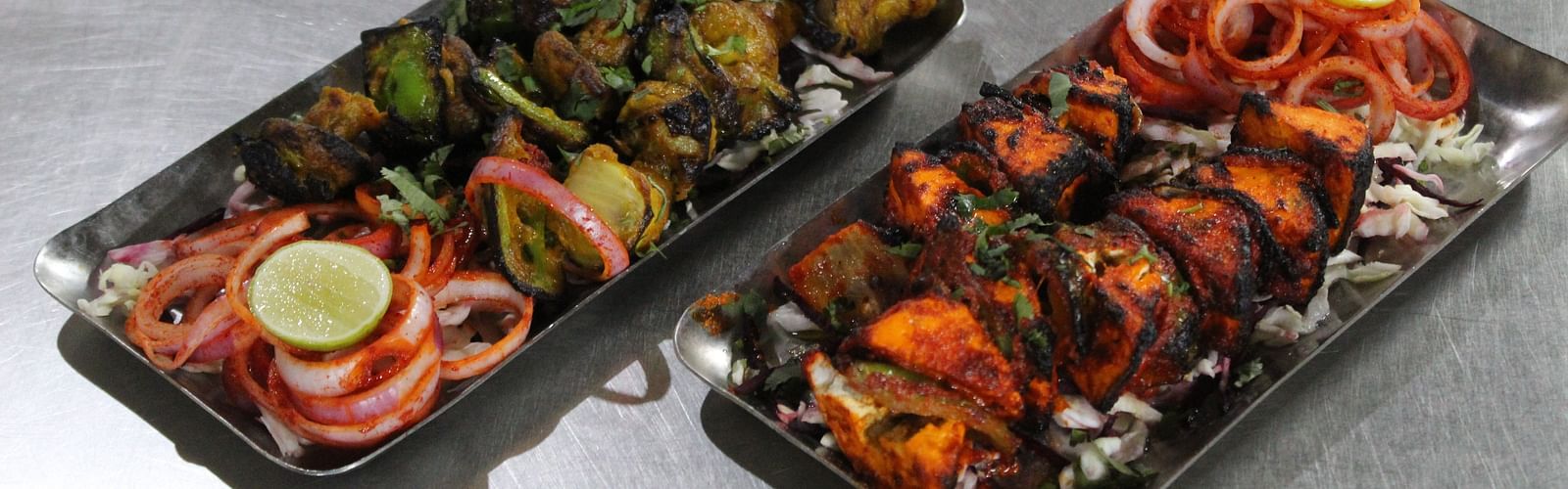 Two platters of grilled tandoori dishes on a stainless steel counter top at Dagshai Manor Kasauli - Inde Hotels.