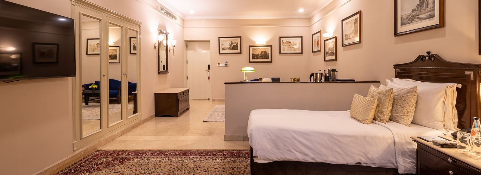 Side view of the Grand Luxury Twin Bed Room at The Claridges New Delhi, showcasing a spacious layout with framed photos on the wall and an elegant lighted ceiling
