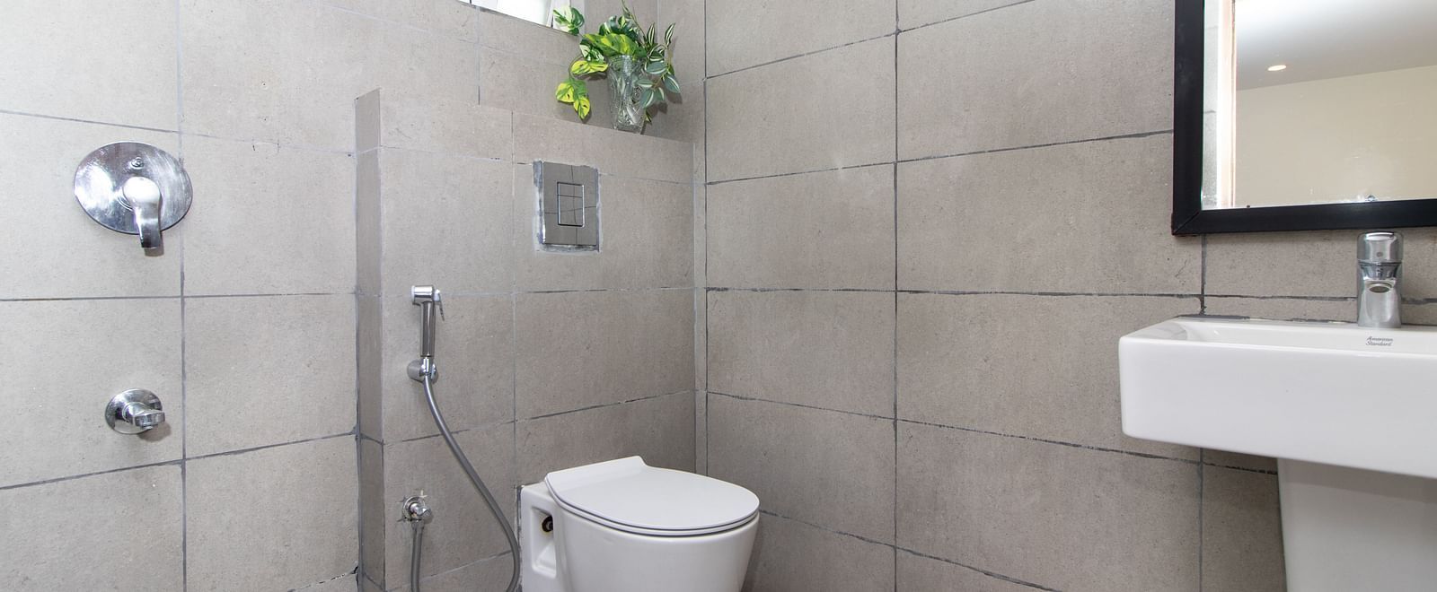 A bathroom with a white toilet, sink, shower controls, and light-coloured tiles - Sanctum Suites Richmond Road, Bangalore