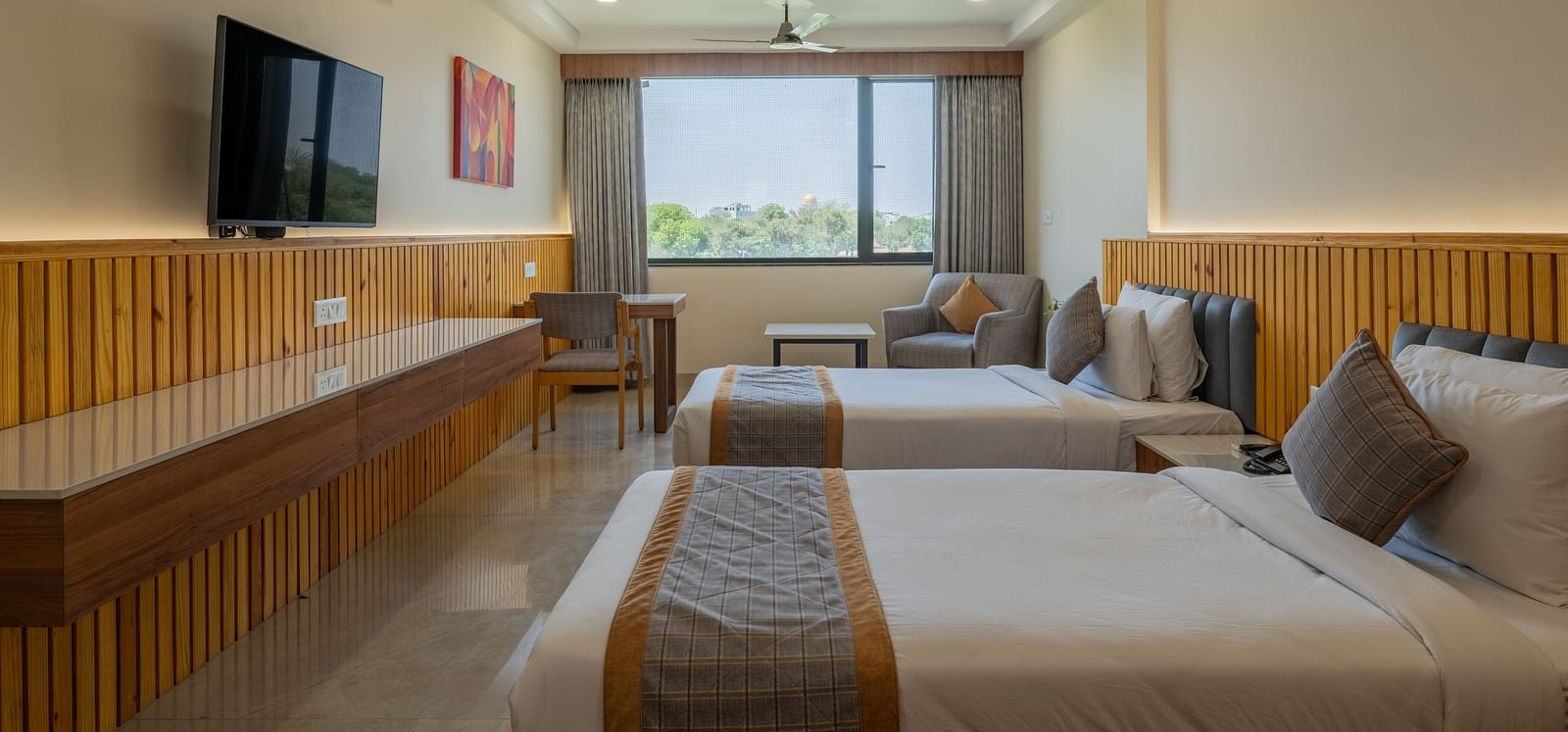 A bedroom at Hotel Highway King, Bagru, with desk, television, large window, ceiling fan, and bedside tables.