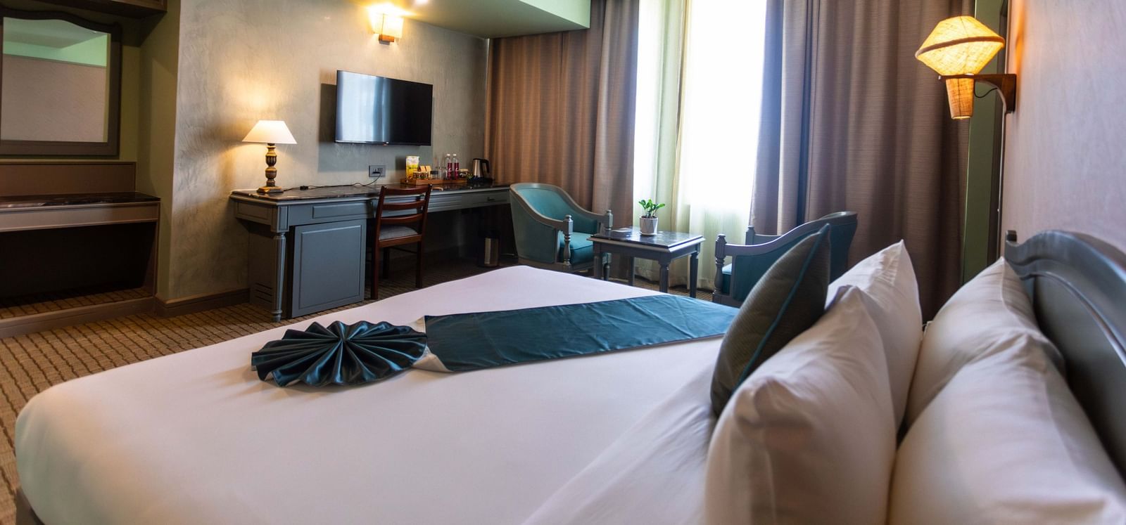 A guest room at Shilton International, Kochi, with a bed, TV, work desk, and seating area.