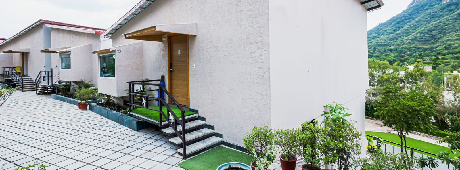 Outside view of Sajjan Villa featuring plants and flower pots and a pavement leading to other rooms and villas.