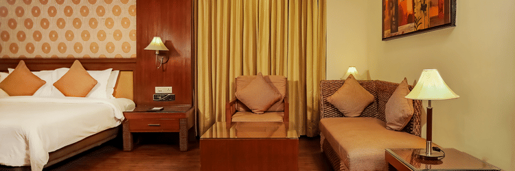 A bedroom with a king bed and a sitting area with wall mounted painting.