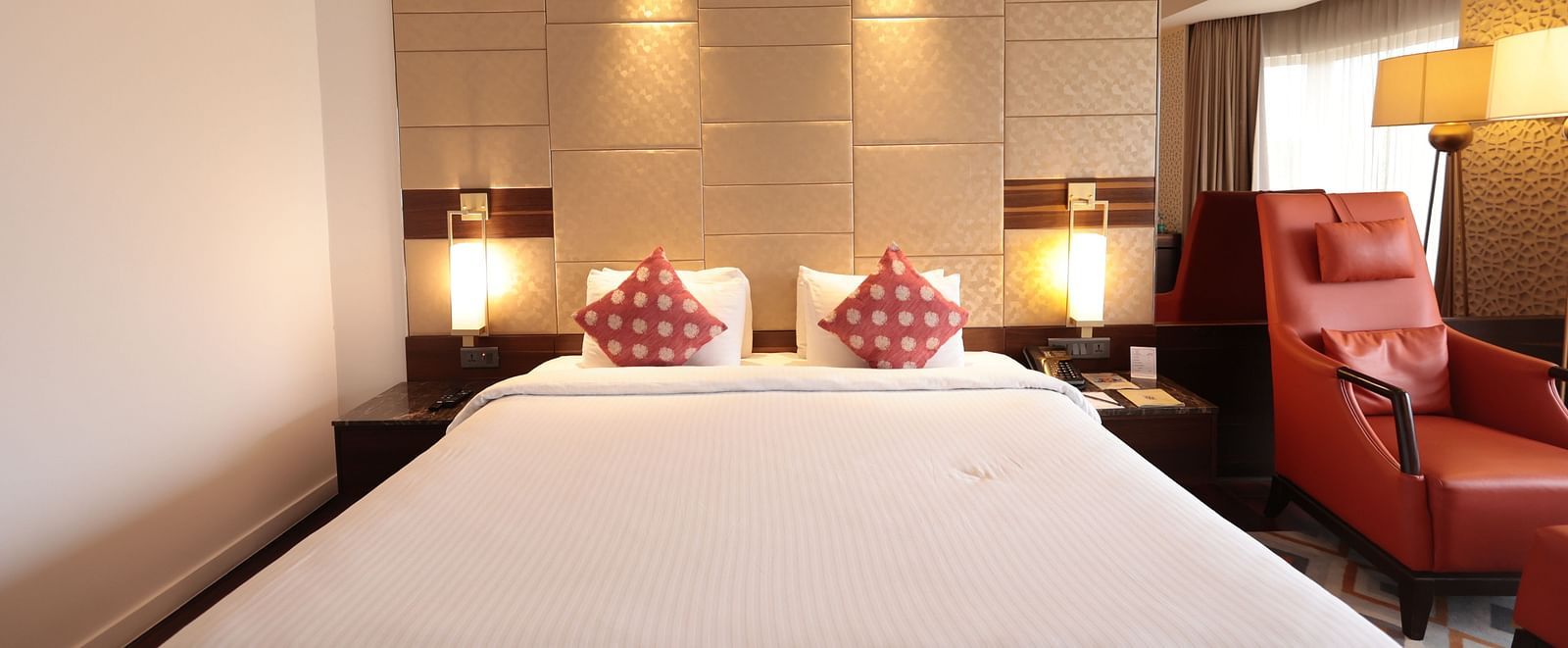A front view of a spacious bed with bedside tables and lamps on both sides, and a cushioned chair on one side | Cenneys Gateway