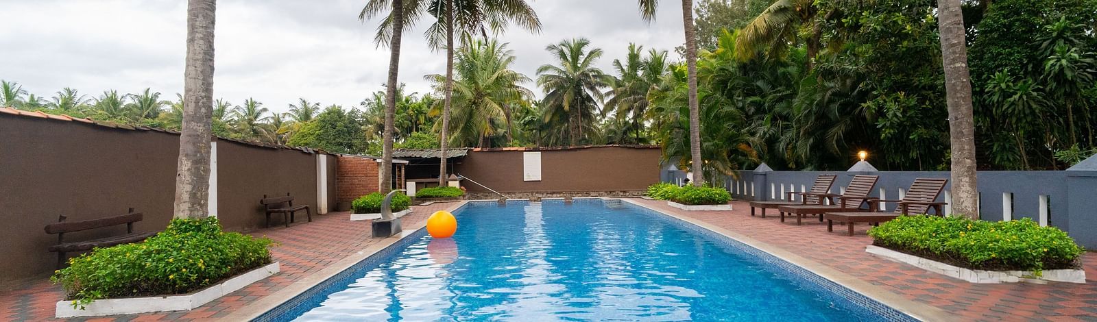 A swimming pool with trees around it at Parampara Resort & Spa, Kushalnagar.