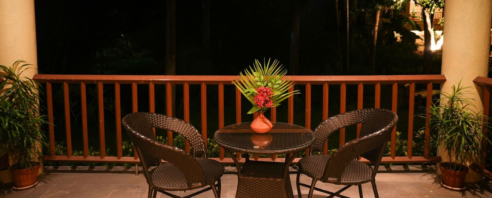 Night-time view of the balcony in the One-Bedroom Suite at Vedic Village Spa Resort, with lounge chairs and wooden railing.