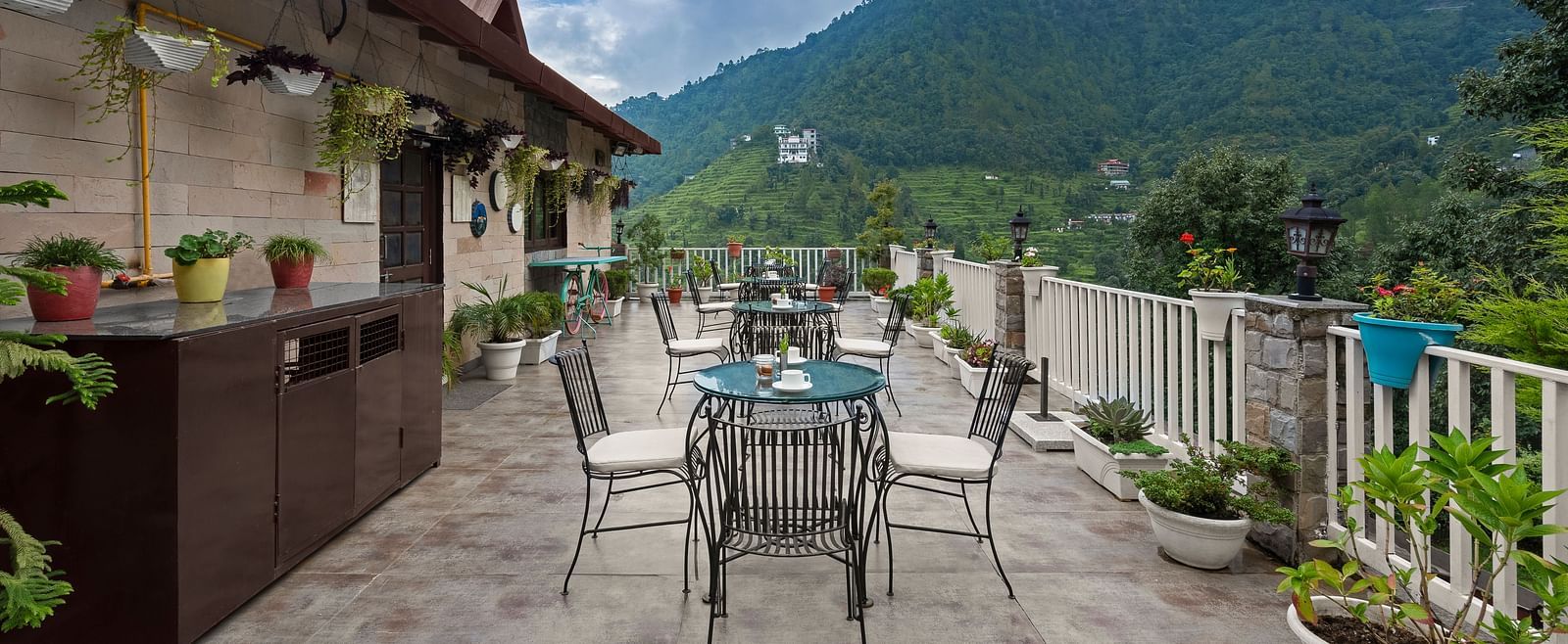 Rooftop dining area with mountain views under a cloudy blue sky, at BluSalzz Collection - Suvaasa Resort, Ramgarh.