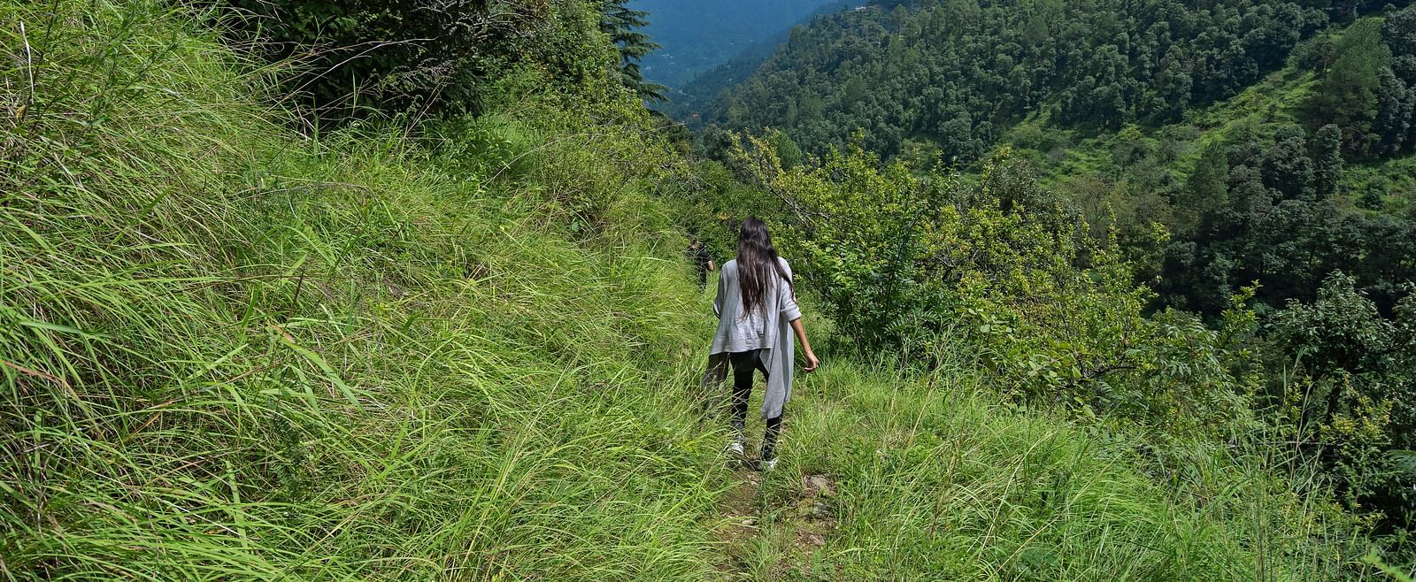Couple trekking through a grassy trail surrounded by mountains and forest, at BluSalzz Collection - Suvaasa Resort, Ramgarh.
