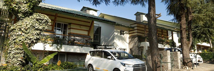 An facade image of a Lamrin Norwood Green, Palampur surrounded by trees and a car is parked in the frontyard