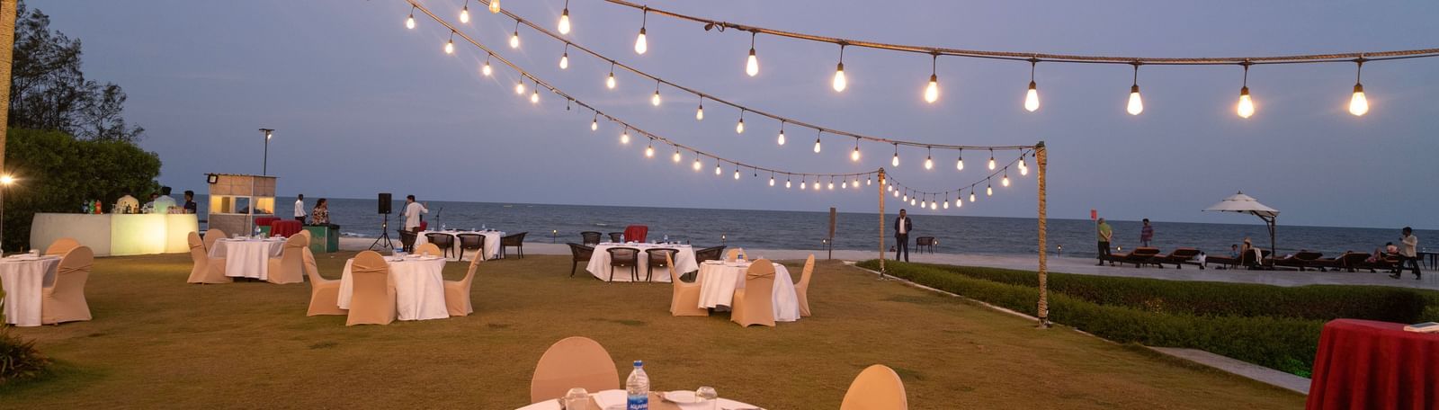 Round tables with white chairs set up on a lawn under string lights - Kaldan Samudra Palace