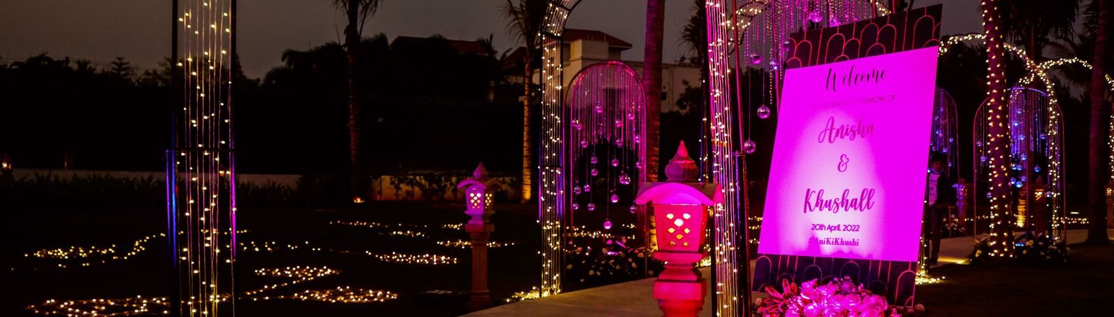 The entrance to the Sangeet of ANisha & Kushaal featuring arches filled with lights and a singboard with the name of the event and the groom and bride at the Lawn of Kaldan Samudhra Palace