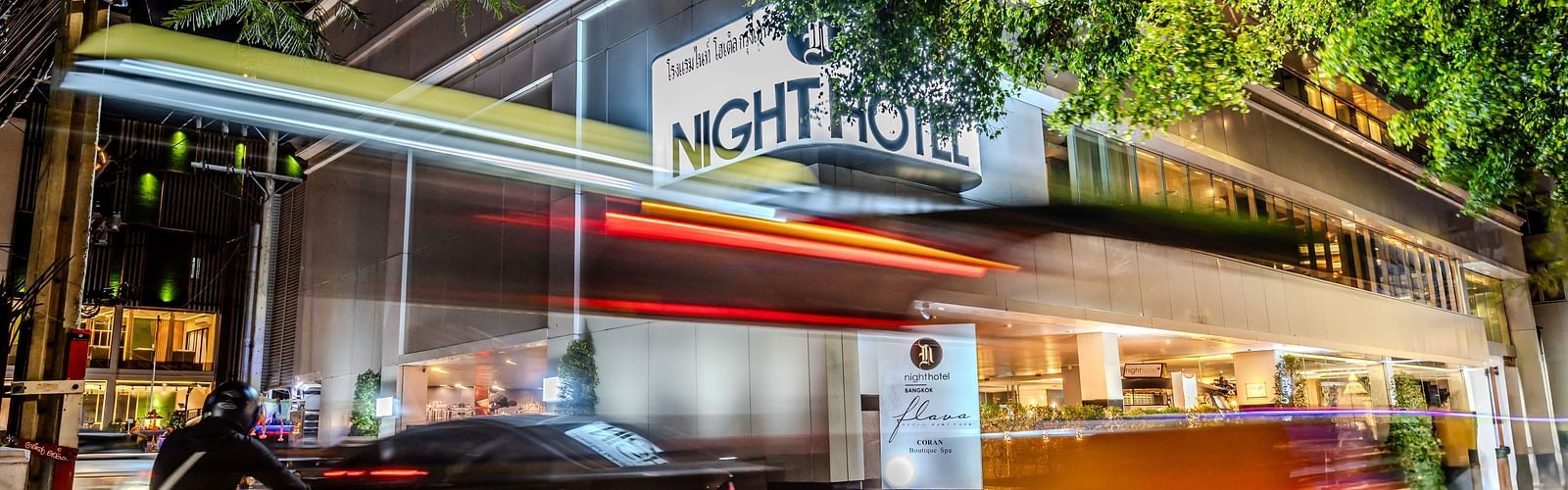 A picture showing Night Hotel Bangkok's Facade with vehicles travelling on the road.