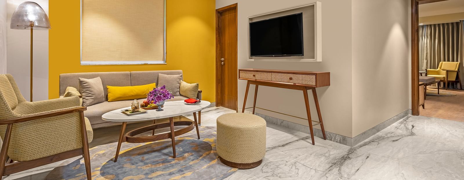The room features a comfortable sofa with colourful pillows, a round coffee table, A floor lamp stands beside the sofa, providing ambient lighting.