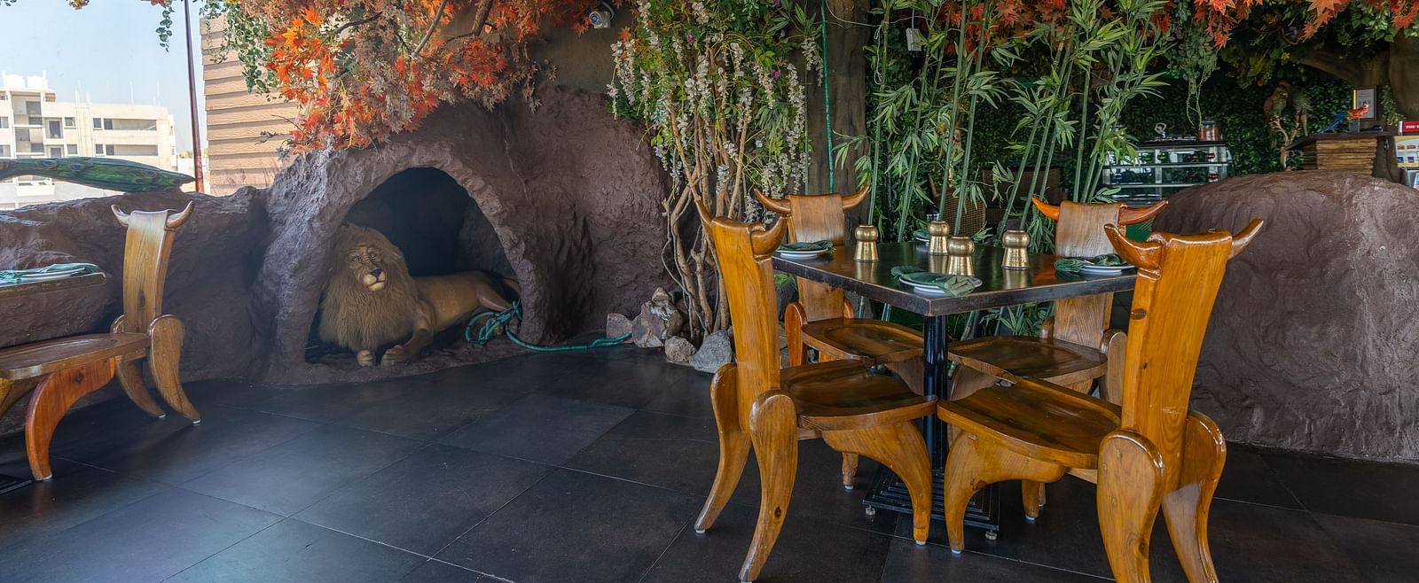 An image of a restaurant decorated with trees featuring several chairs and tables - The President Hotel, Hubli