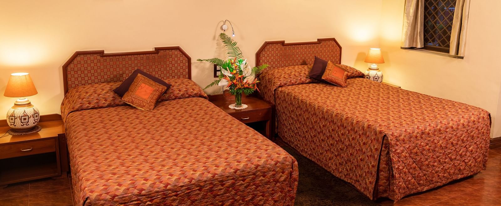 Cosy bedroom with twin beds, warm lighting, and simple decor on the walls - BluSalzz Collection - Tranquil Resort, Wayanad