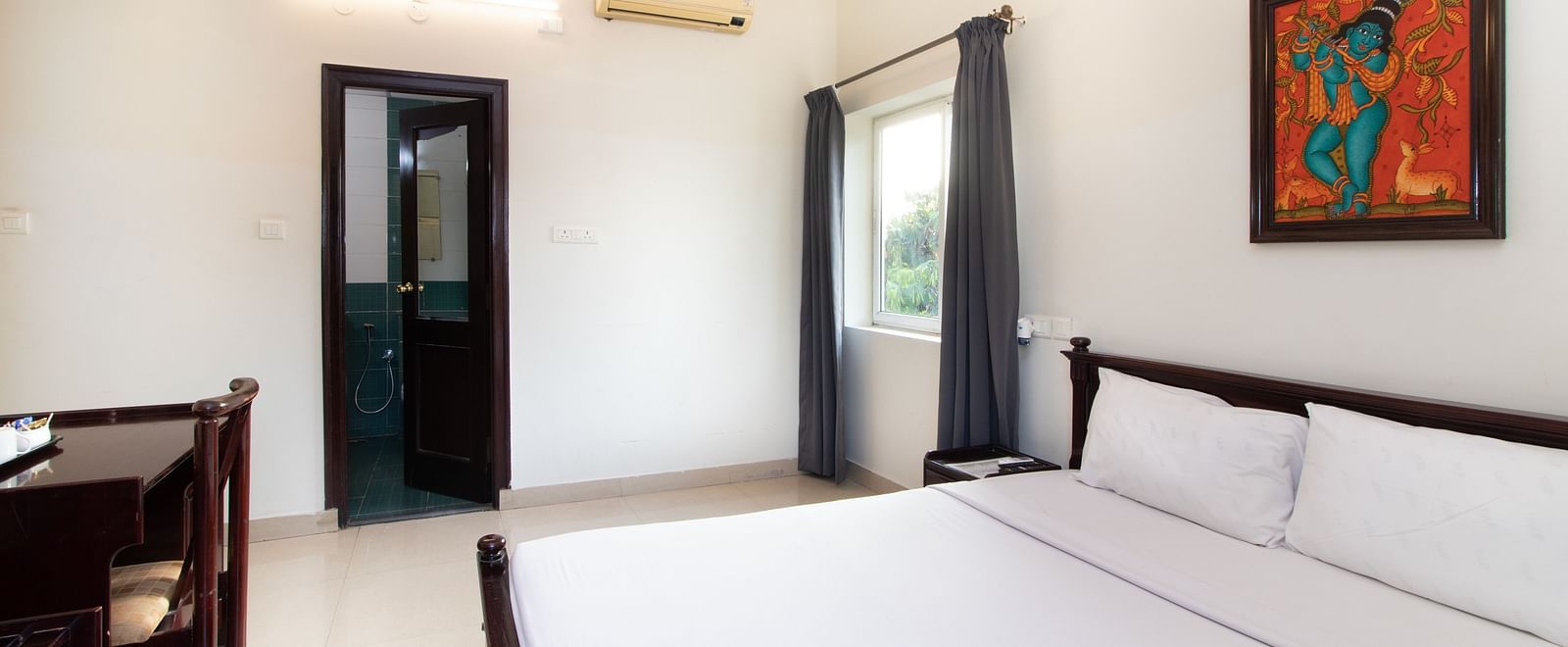 A well-lit room showcasing a double bed with white bedding, a farmed artwork, and a dedicated desk area at Sanctum Suites Indiranagar, Bangalore.