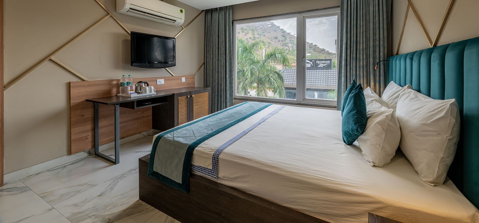 A spacious guest room with a large bed, TV, and outdoor view at Hotel Highway King Shahpura.