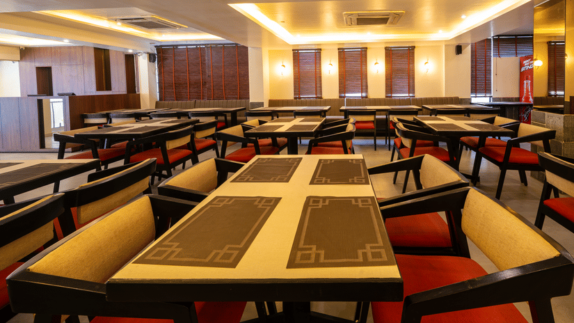 A warmly lit dining hall at VITS Select, Bengaluru, showing rows of long tables set with placemats and multiple upholstered chairs.