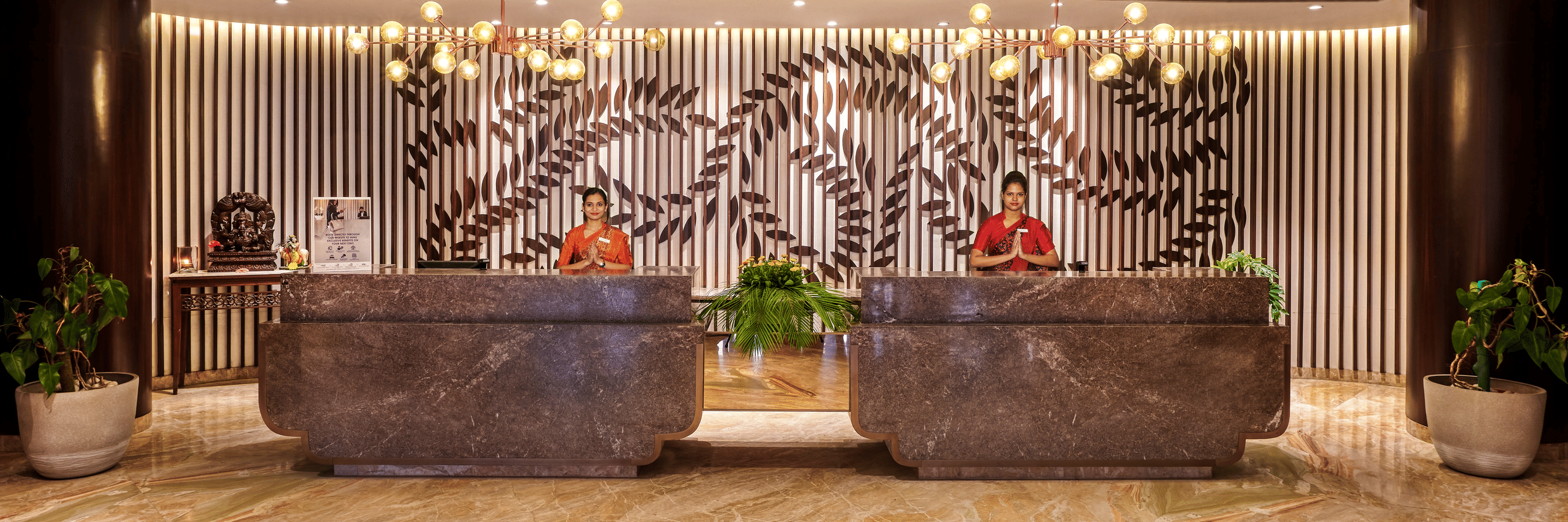 Two receptionists at the lobby of Pride Premier Nagpur desk doing namaste which is a way to greet guests.