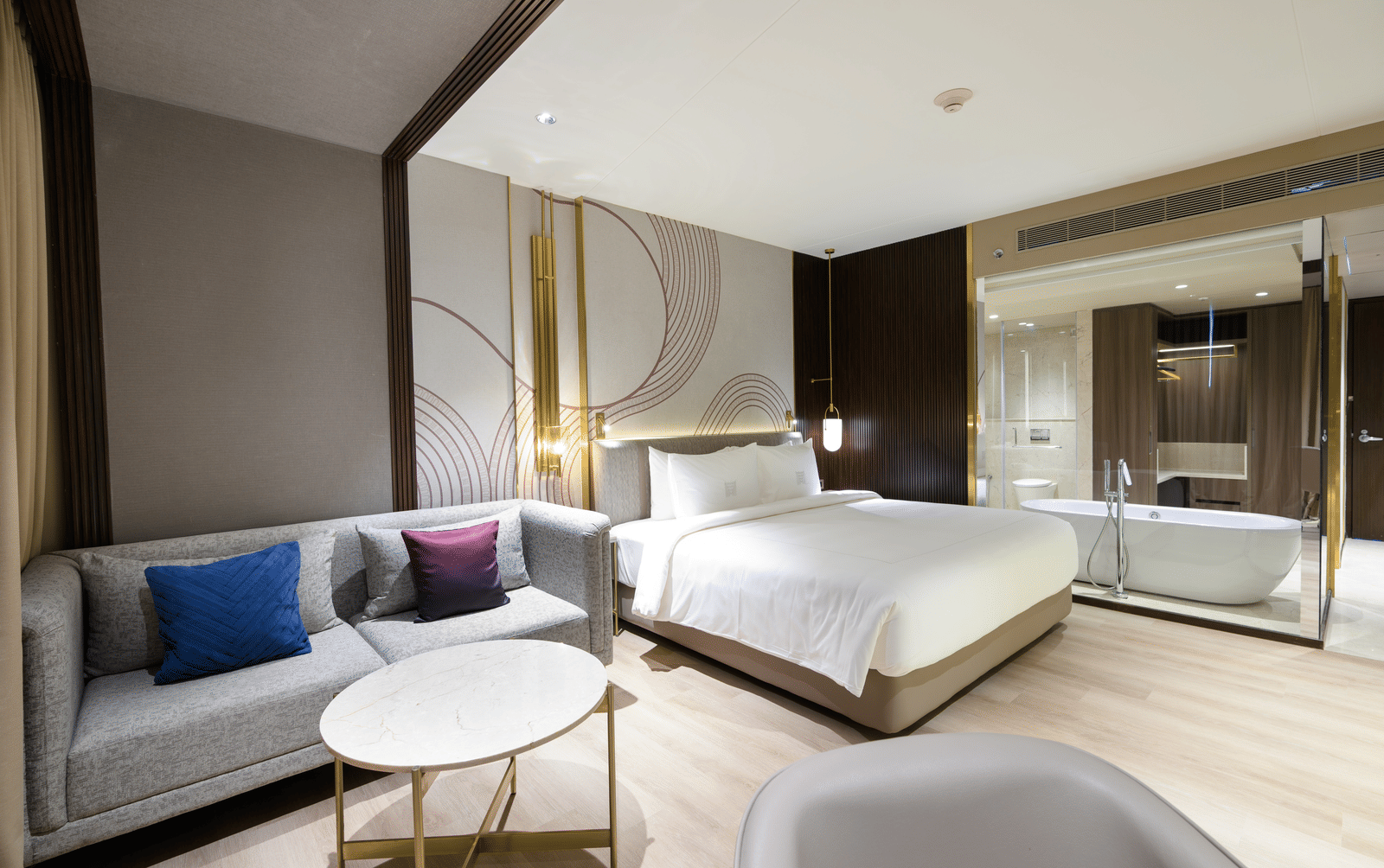 Room featuring a bed, a sofa next to it and a glass wall separating the bedroom from the bathroom bathtub at Merlis Hotel, Coimbatore