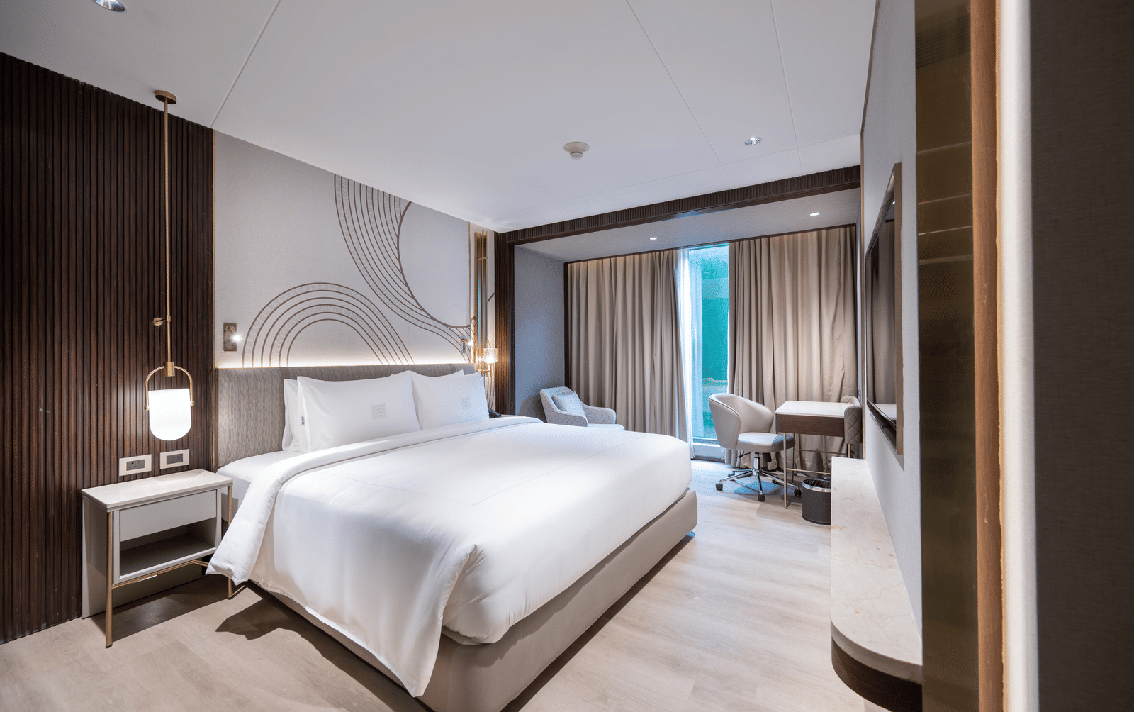  A contemporary hotel bedroom featuring a large double bed, modern lighting, and a small desk area at Merlis Hotel, Coimbatore.