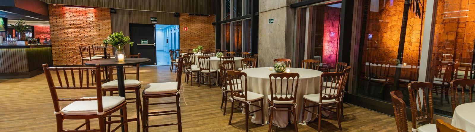 An empty event space with high-top tables and chairs, illuminated by warm lighting.
