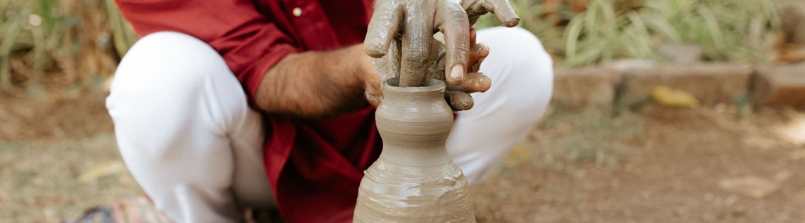 A person moulding clay on a pottery wheel placed outdoors at Daksh Eden Greenz, Sasan Gir.