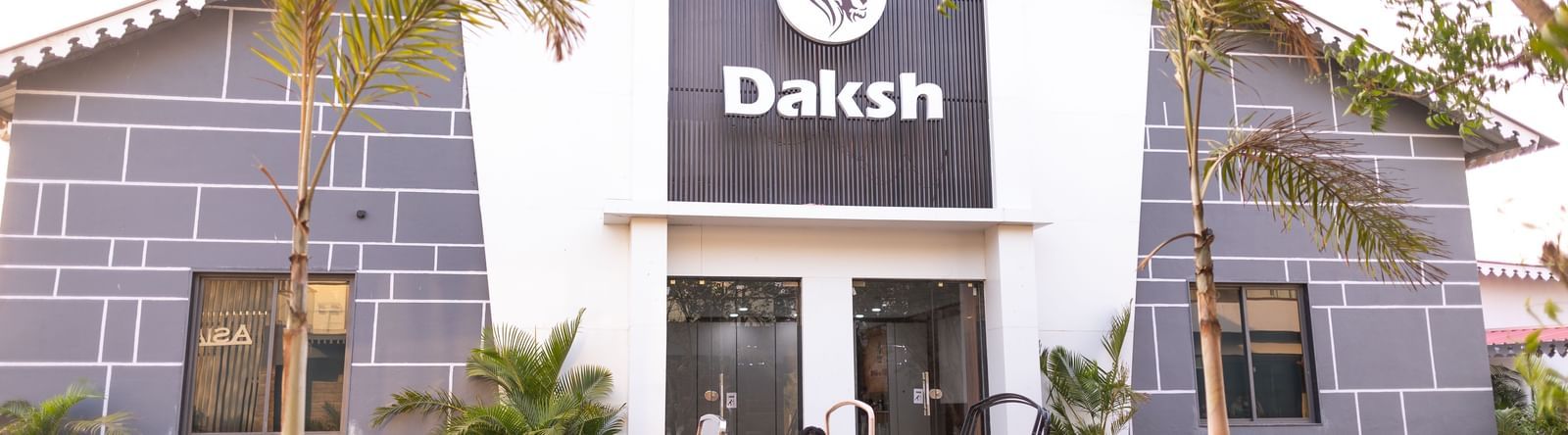 A vintage car stopped behind potted plants, with the exterior of a building standing tall in Daksh Eden Greenz, Sasar Gir.
