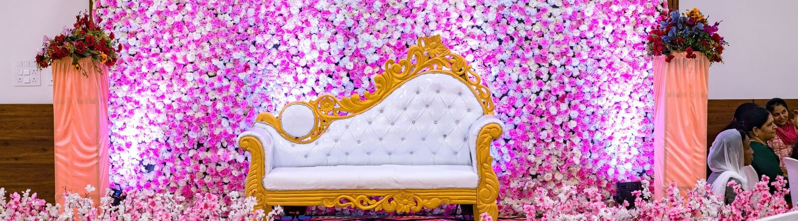 Floral wedding stage with ornate golden seating at Daksh Hotels and Resorts, set against a wall of pink and purple blooms.