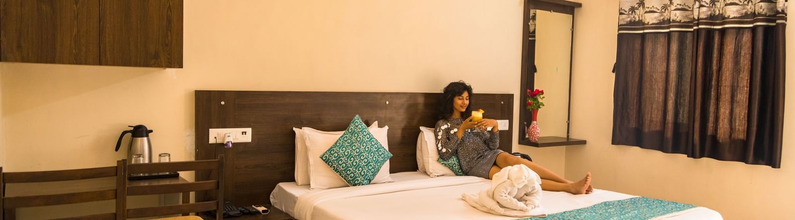 A guest room with a double bed, chairs, and dressing area, with a woman seated at Daksh Resort & Amusement Park.
