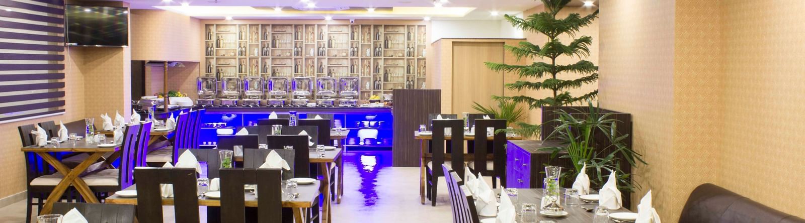A hotel restaurant with set tables, dark chairs, and blue ambient lighting | Daksh The Madhuvan Suites