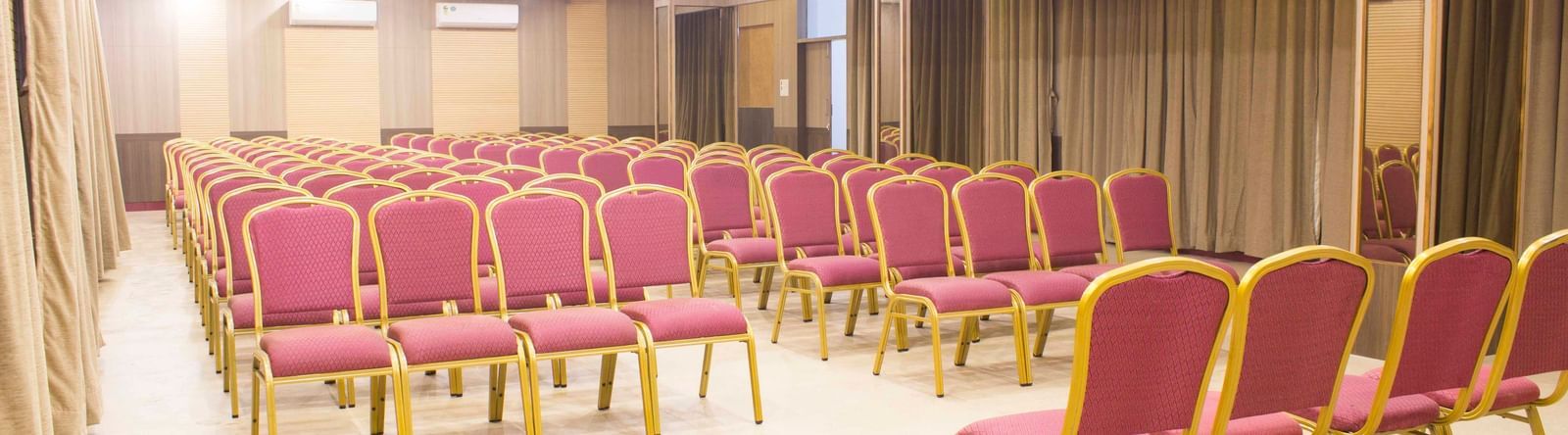 A wide shot of a banquet hall with multiple rows of empty pink and gold chairs. | Banquet Hall | Daksh The Madhuvan Suites