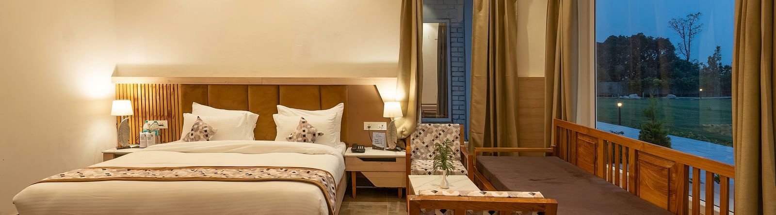 A cosy hotel room with a king-size bed, a seating area, and a view of the lush green outdoors.
