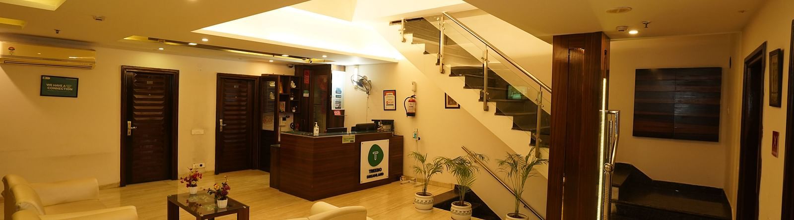 Lobby at Hotel Dreamland, Chandigarh featuring a curved, light-coloured sofa, a dark wood reception desk, and a staircase leading to the upper floors.