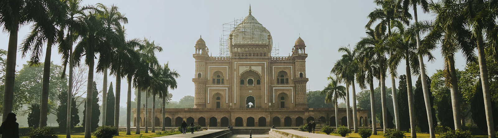 A serene view tomb of Safdarjung in New Delhi, India, framed by tall palm trees and reflected in the water of the frontal canal on a clear day