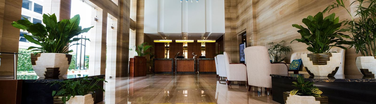 An expansive lobby with ample of natural light coming from outside of the hotel featuring a reception desk at the far end of the lobby - Ramada by Wyndham, Ghaziabad, Vasundhara