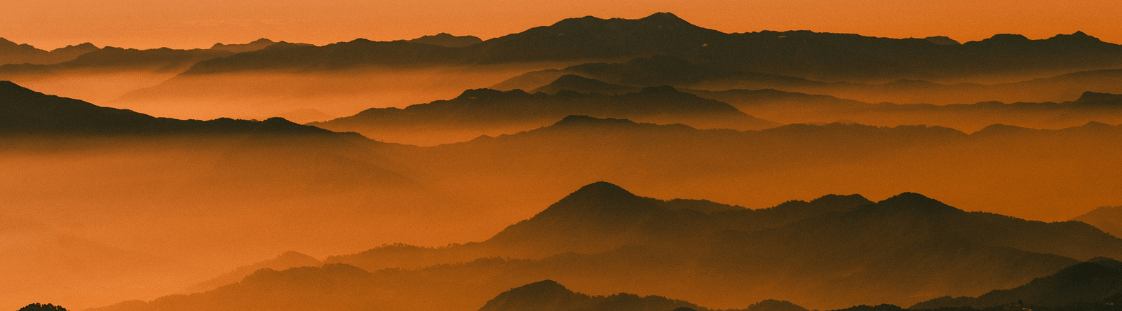 Hill tops one after another being submerged in the clouds with an orange hue in the sky
