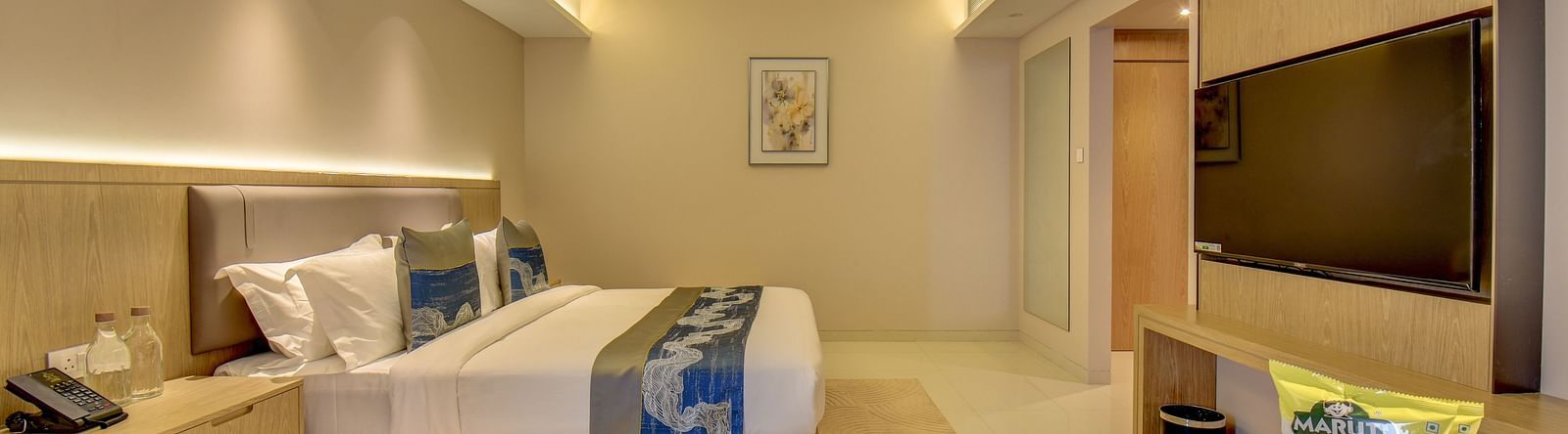 A well-lit Deluxe King room at The SSK Solitaire Boutique Hotel & Spa, Gangapur Road - Nashik featuring a king size  bed, two armchairs, a small table, and a work desk with a chair.