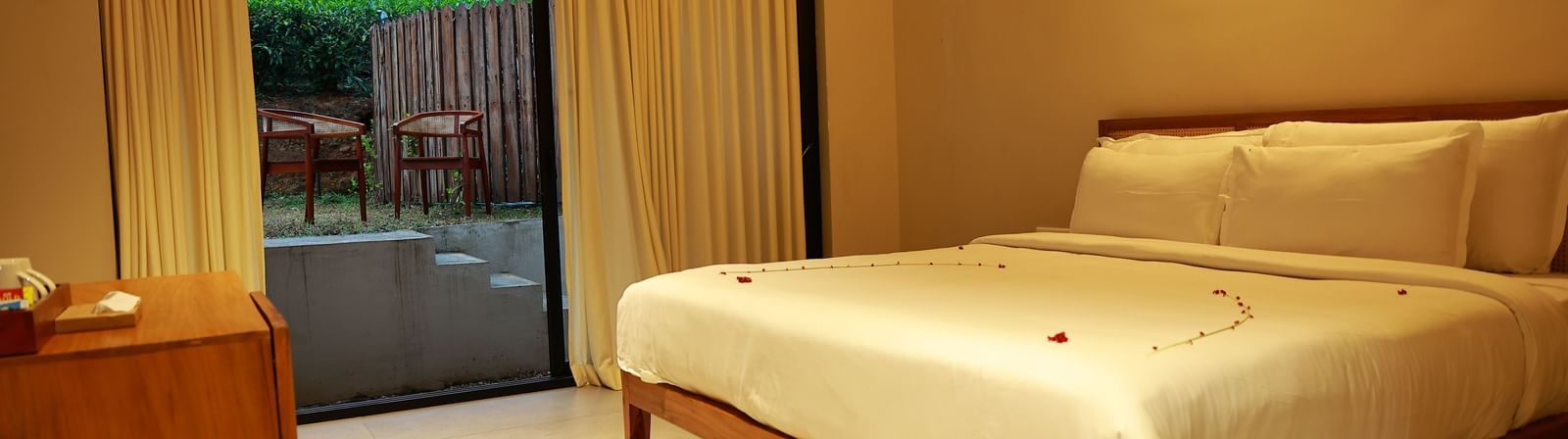  A hotel room at Vaasta Vagamon featuring a bed with subtle petal decor, a wooden cabinet, and a sliding door leading to an outdoor patio.