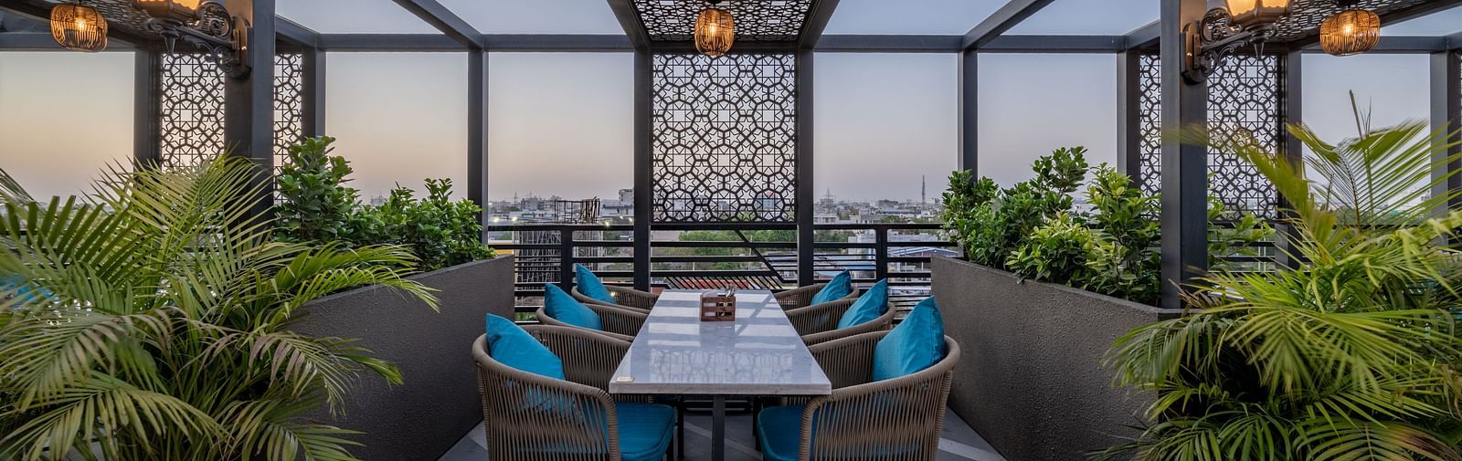 Central rooftop dining set up under decorative latticework surrounded by greenery at Hotel Highway King, Jaipur.