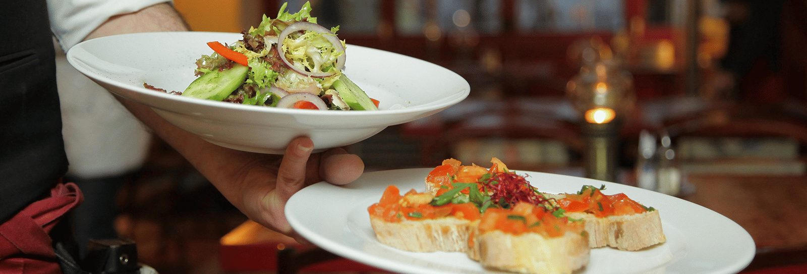 a person in a restaurant holding two plates with delicious cuisines in it that are well plated