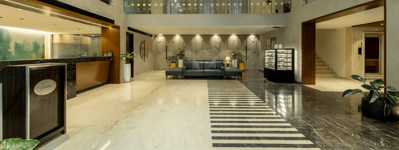 A wider view of the lobby and reception area at the Citrine Hotel, with a staircase leading to an upper floor.