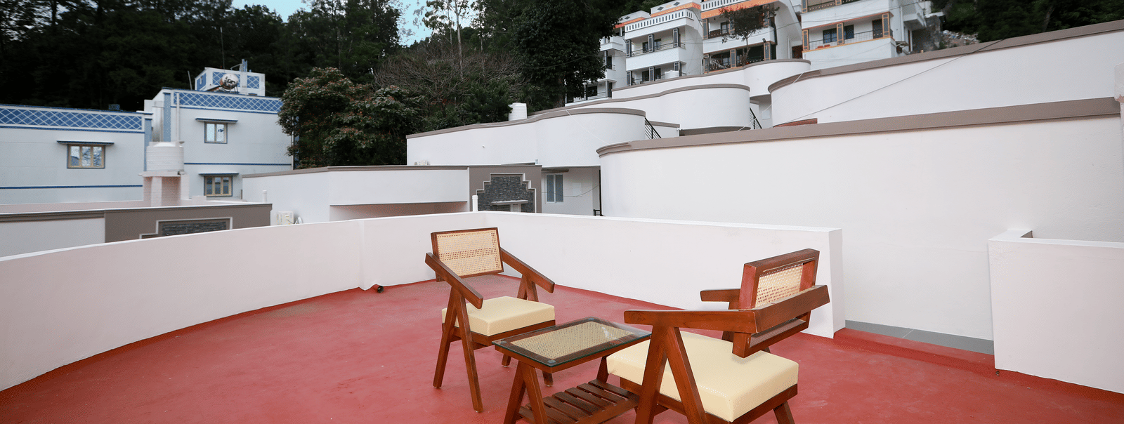 The terrace area with 2 arm chairs and a coffee table with a scenic backdrop of lush green trees and a blue evening sky at WOW Naturefull Resorts, Yercaud.