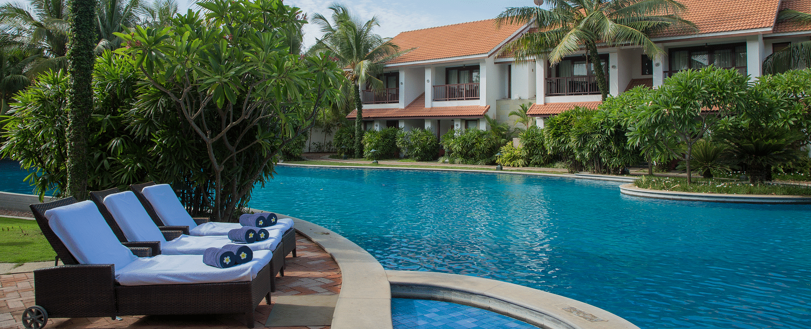 Luxury resort with a swimming pool, lounge chairs, and tropical greenery at GRT Hotels.