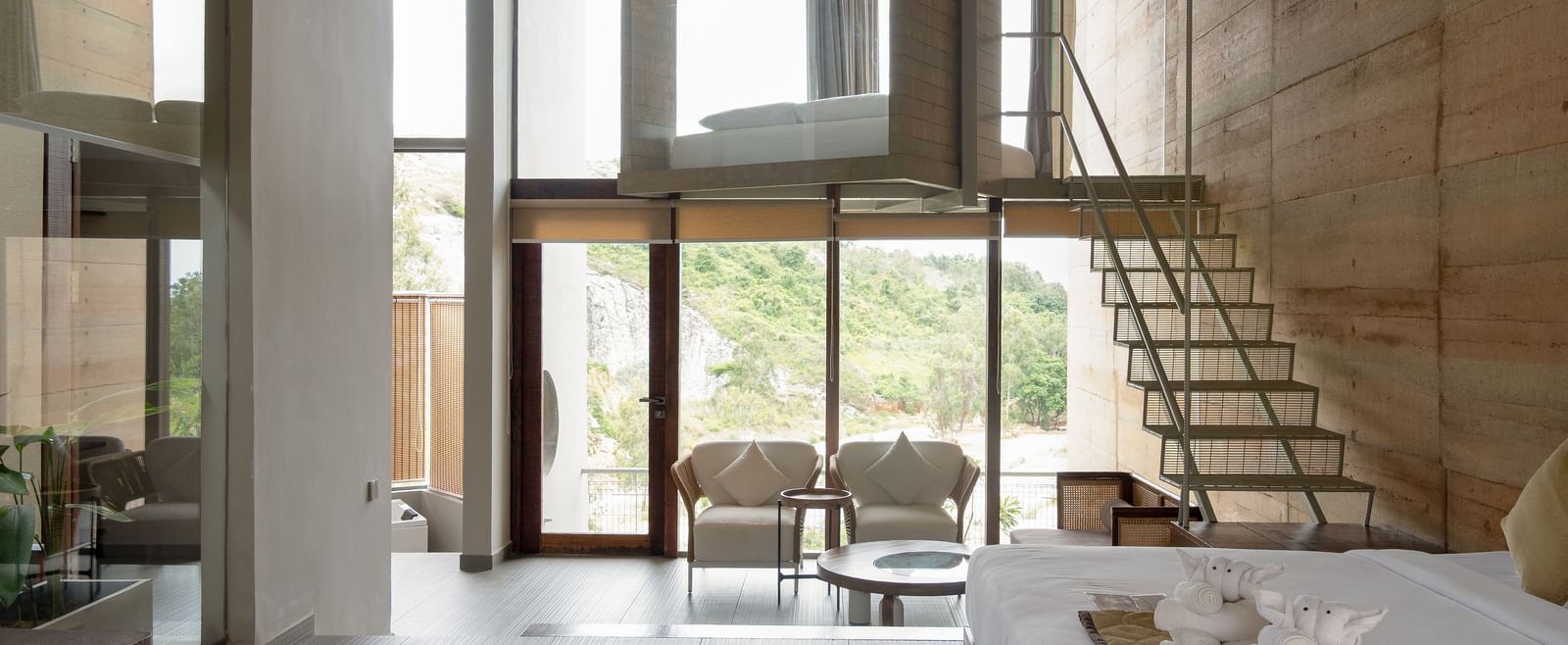 Interiors of two storey building. Ground floor has a bed and a seating area with sofa chairs and a centre table. The stairs leading to the top also has another bed placed at RD's Nature Retreat, Bangalore