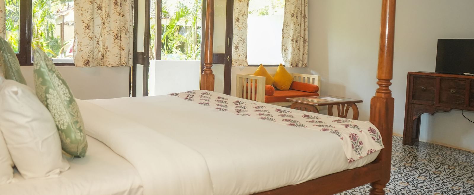 Room with a four-poster bed, sheer curtains, cushioned chair, and large windows opening to greenery at De Soul Santé, Morjim.