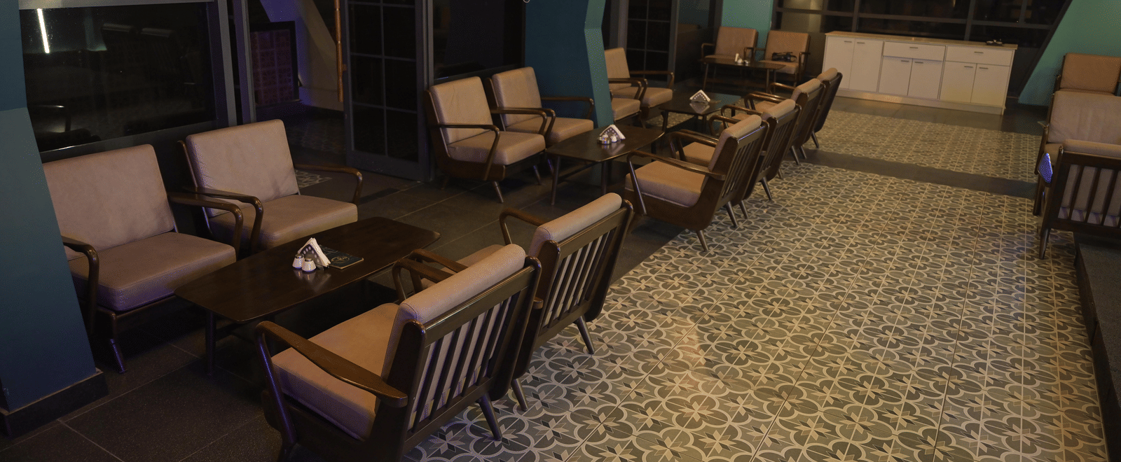 A side-angle view of the bar’s seating area with cushioned sofas set beside large glass windows at Hotel Sonar Bangla Mayapur.